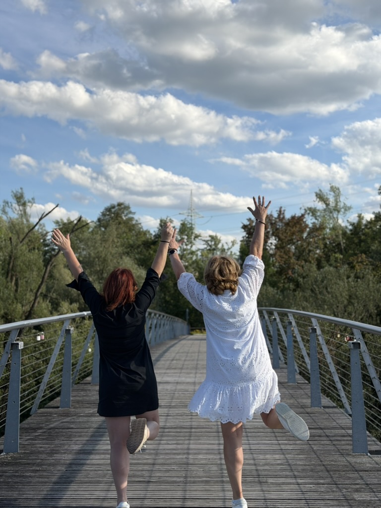 Zwei Frauen springen auf einer Brücke, ihre Hände berühren sich
