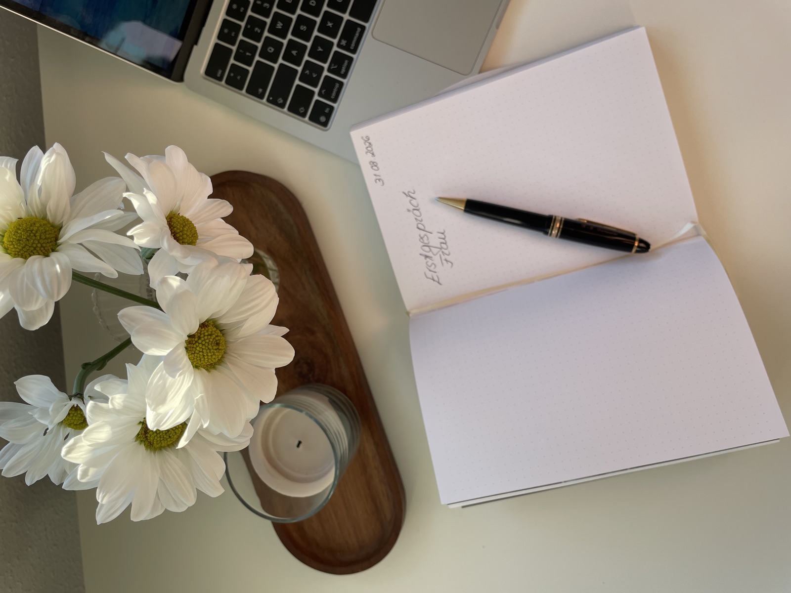 Notizbuch mit der Aufschrift „Erstgespräch“, Stift und Blumen auf einem Schreibtisch